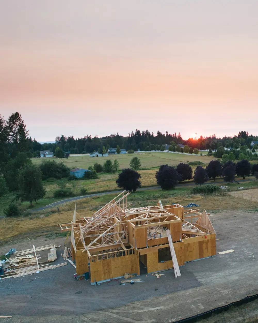A new home being framed on an open homesite at sunset