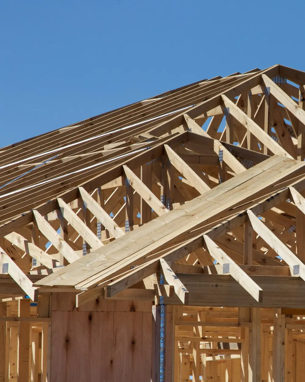 Roof trusses and wall framing going up on a new home against a blue sky