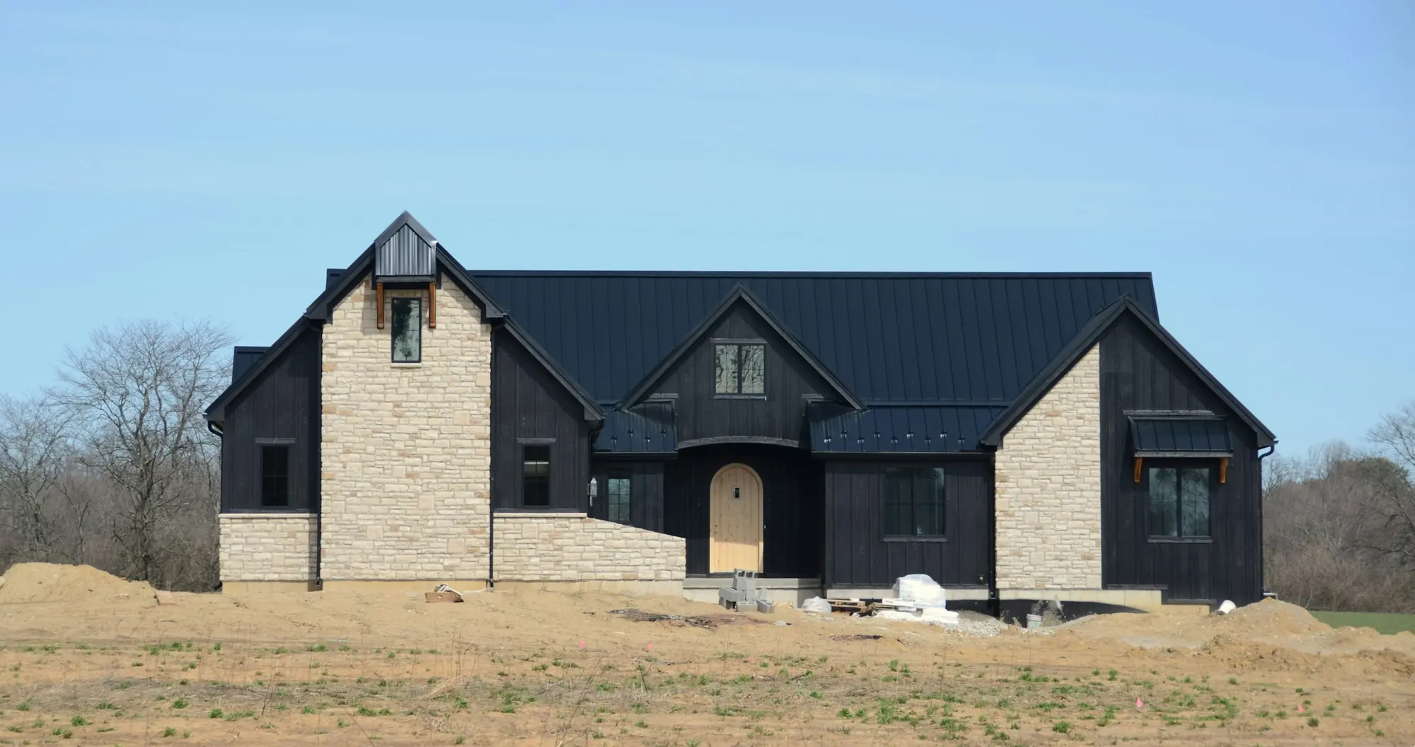 Single-story modern farmhouse with black siding and a stone front on a new homesite