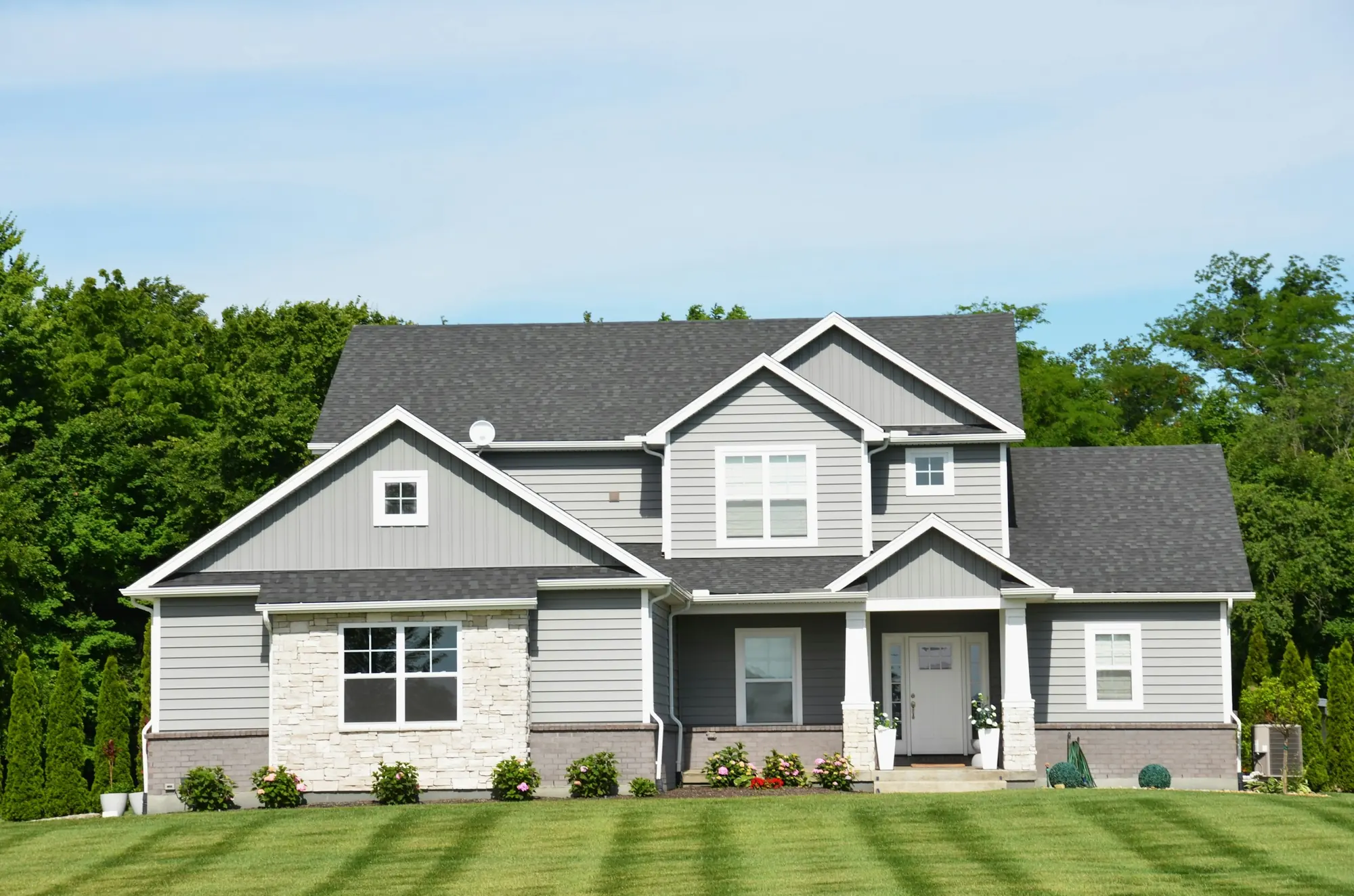 Two-story gray home with a stone base, a covered front porch and a new lawn