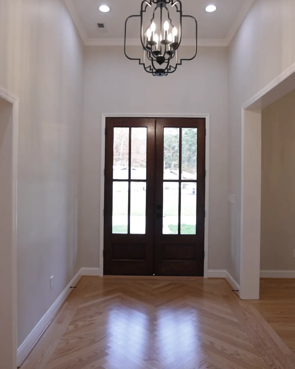 A bright new foyer with hardwood floors, a chandelier and double front doors