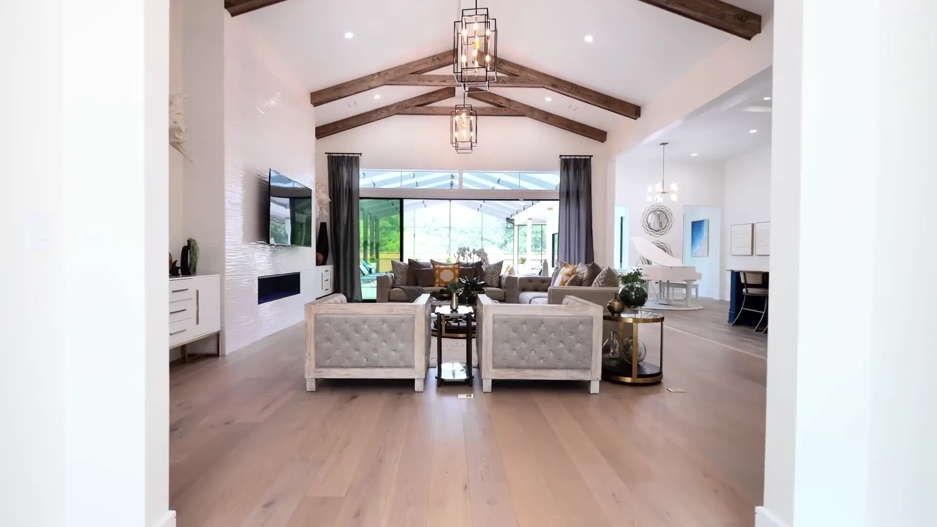 A vaulted great room with wood beams, a chandelier and a wall of glass to the back patio