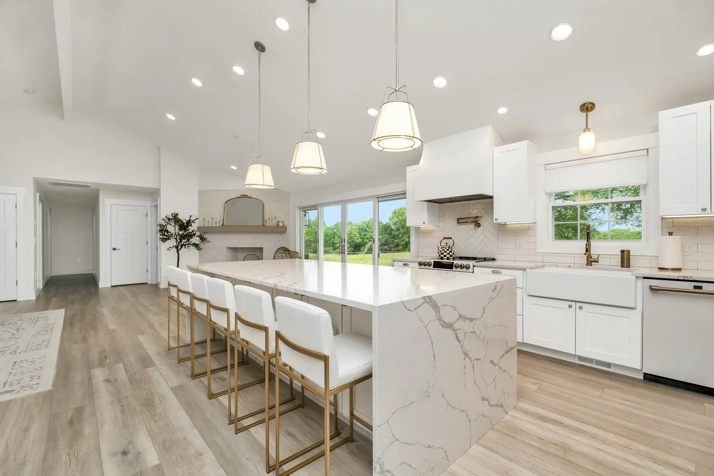White kitchen with a waterfall quartz island, pendant lights and plank floors