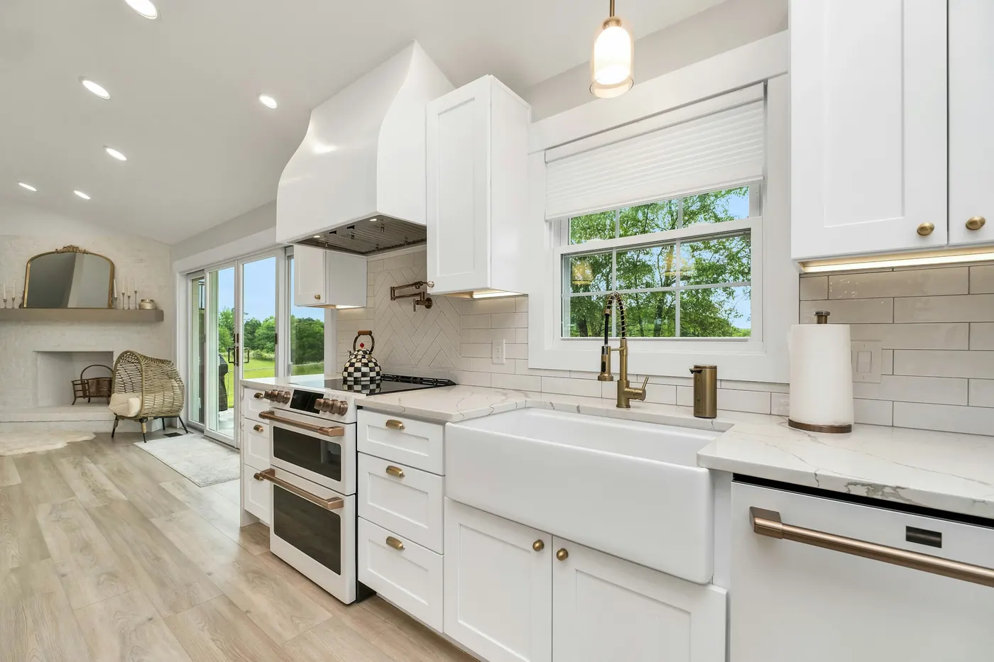 Farmhouse sink below a window, with white shaker cabinets and gold hardware